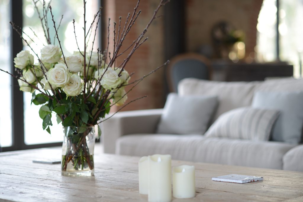 Bouquet de roses blanches et bougies posés sur une table en bois clair dans un salon lumineux et apaisant, symbole du raffinement des séjours Grainedejeune.