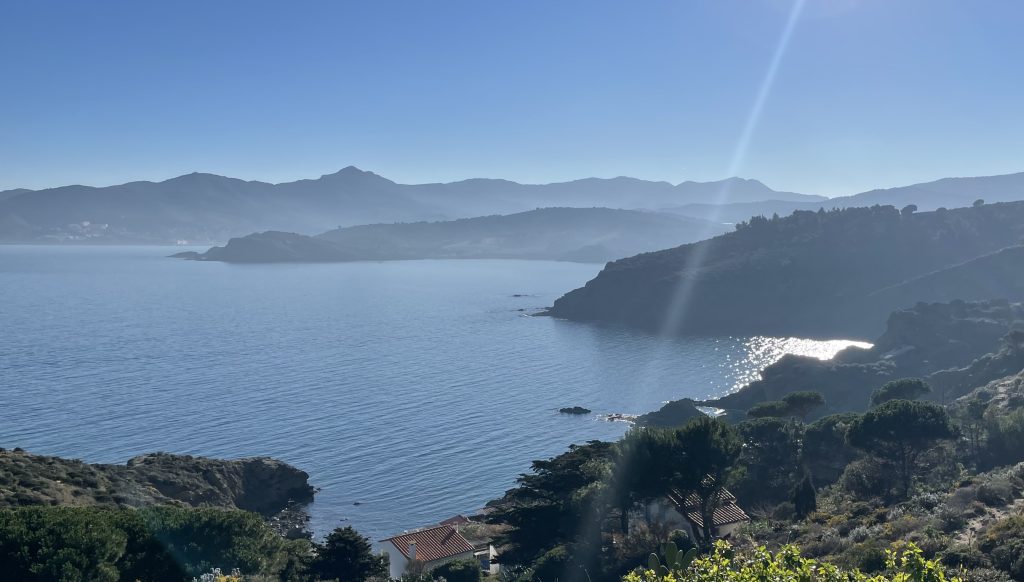 Paysage côtier méditerranéen au lever du soleil, avec mer scintillante et montagnes en arrière-plan, symbole de calme et de beauté naturelle des séjours Grainedejeune.