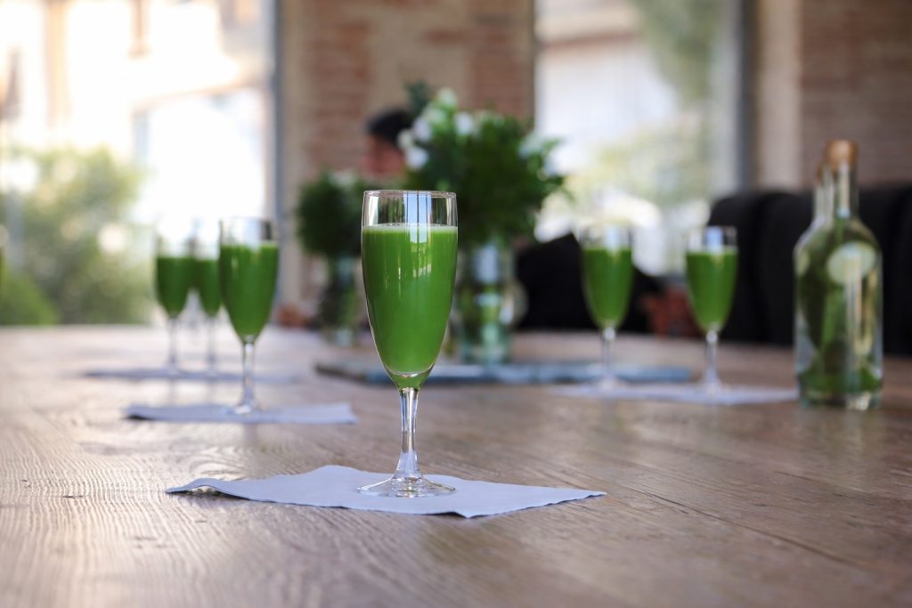 Verres de jus vert alignés sur une table en bois clair, symbole d’énergie, de fraîcheur et de bien-être des séjours de jeûne haut de gamme Grainedejeune.