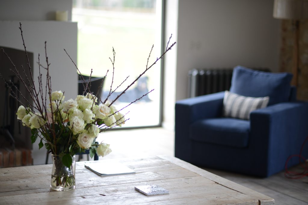 Bouquet de roses blanches posé sur une table en bois clair dans un salon lumineux et apaisant, symbole du bien-être haut de gamme des séjours Grainedejeune.
