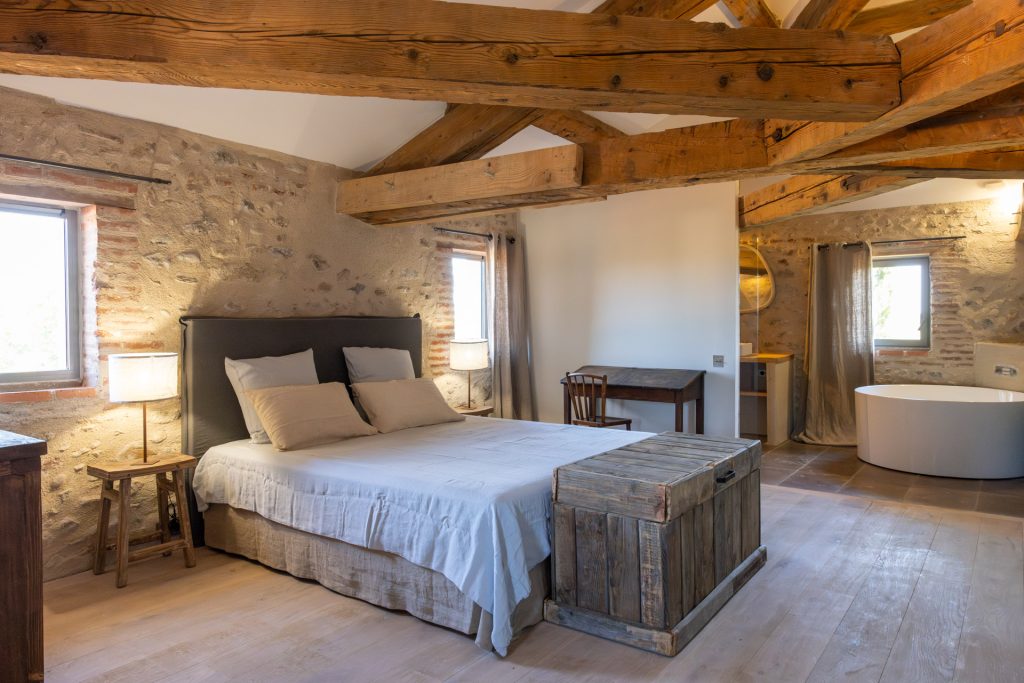 Grande chambre avec poutres apparentes, baignoire et murs en pierre dans un lieu de jeûne haut de gamme Graine de Jeûne