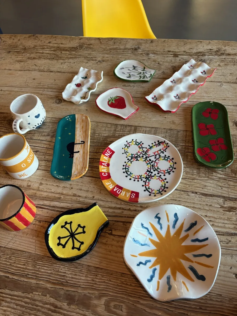 Une quinzaine de pièces de céramique peintes à la main, posées sur une table de bois