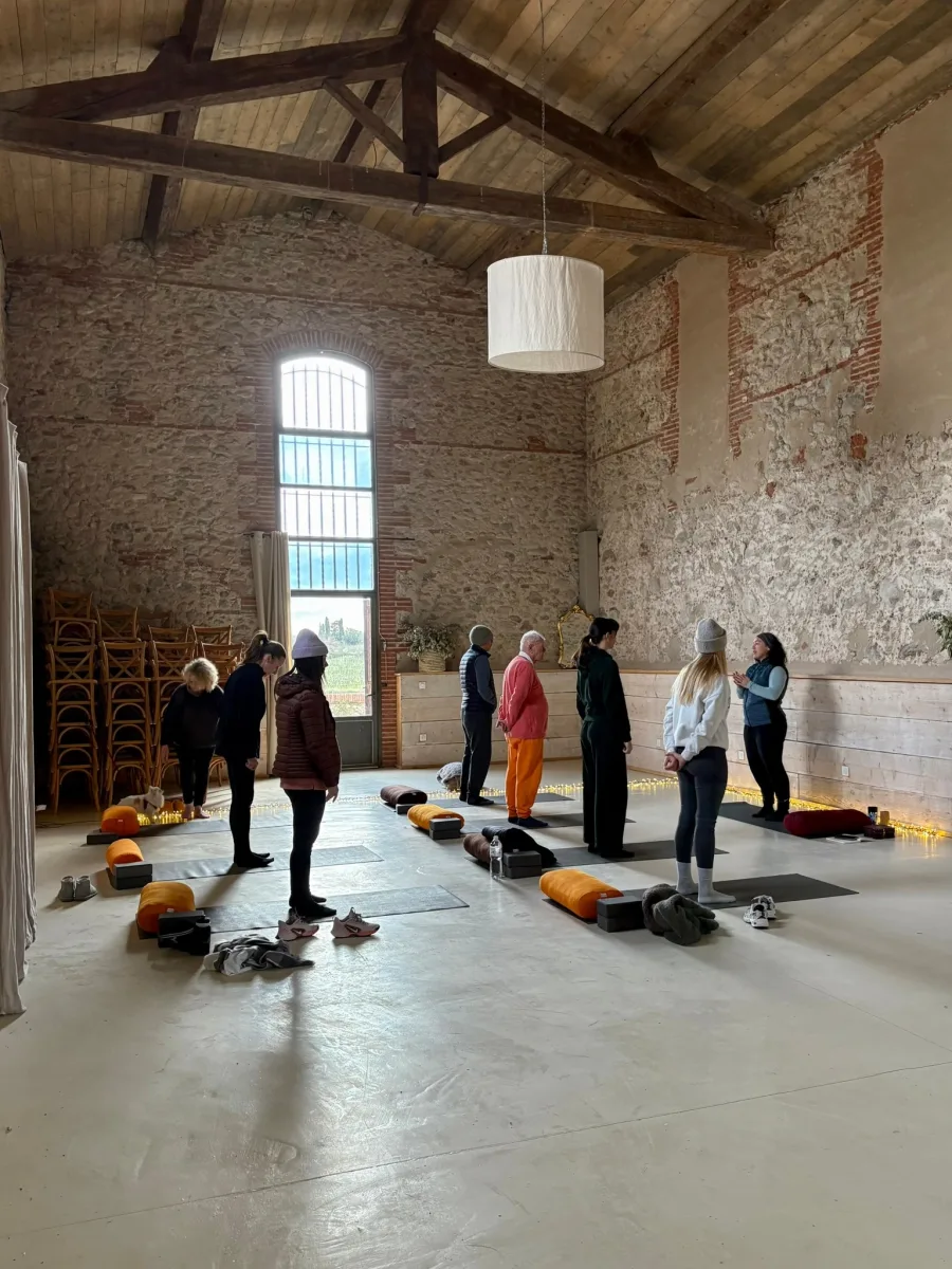 Un groupe debout sur des tapis dans une grande salle voûtée en pierre, devant une haute fenêtre en arc