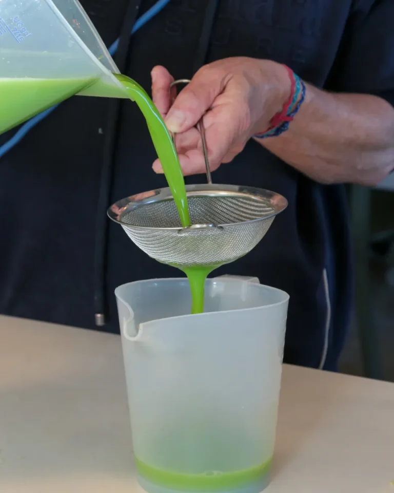 Une main filtre un jus vert à travers une passoire fine au-dessus d'un pichet gradué