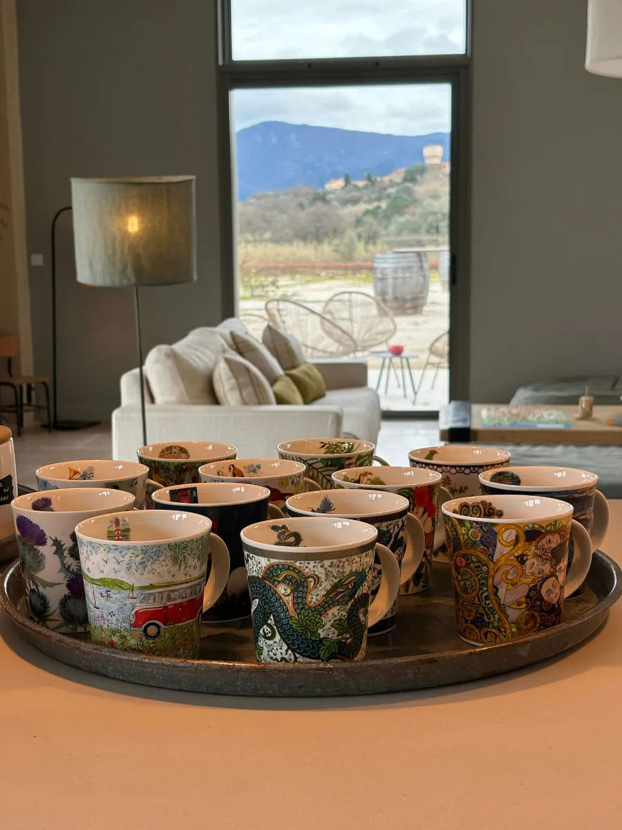 Plateau de mugs colorés et dépareillés, le salon et les montagnes visibles derrière