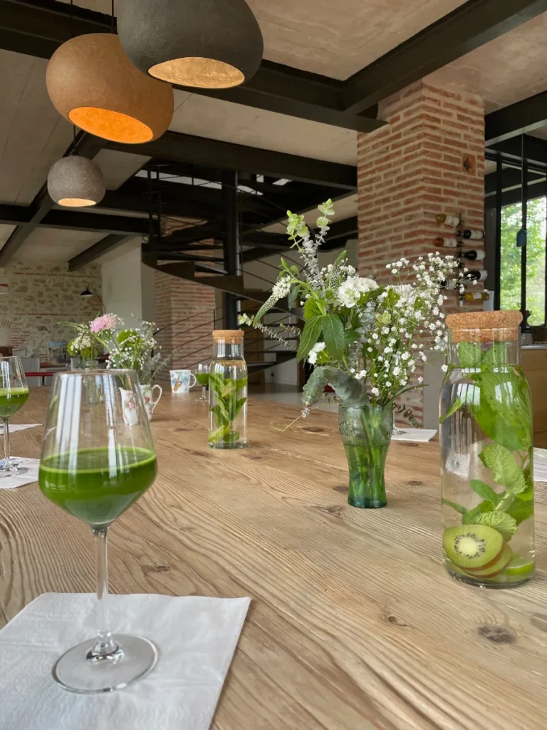 Table en bois dressée avec des verres de jus vert, des carafes d'eau infusée et des bouquets de fleurs blanches