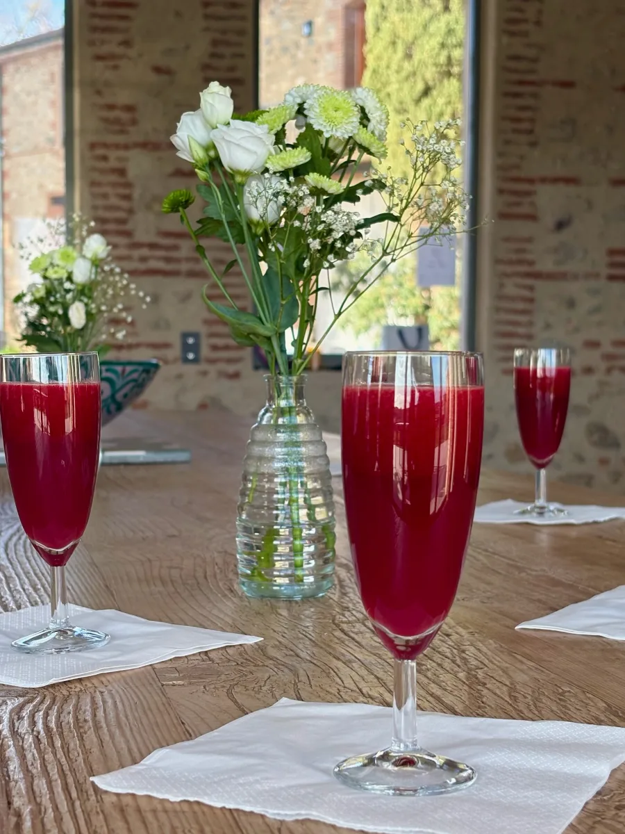 Verres à pied remplis de jus de betterave posés sur une table en bois, près d'un bouquet de fleurs blanches