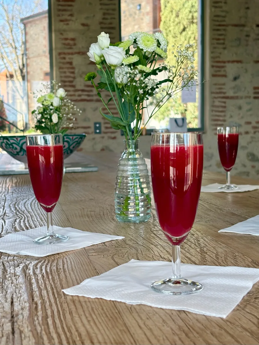 Verres de jus rouge servis sur une table en bois, entourés de bouquets de fleurs blanches