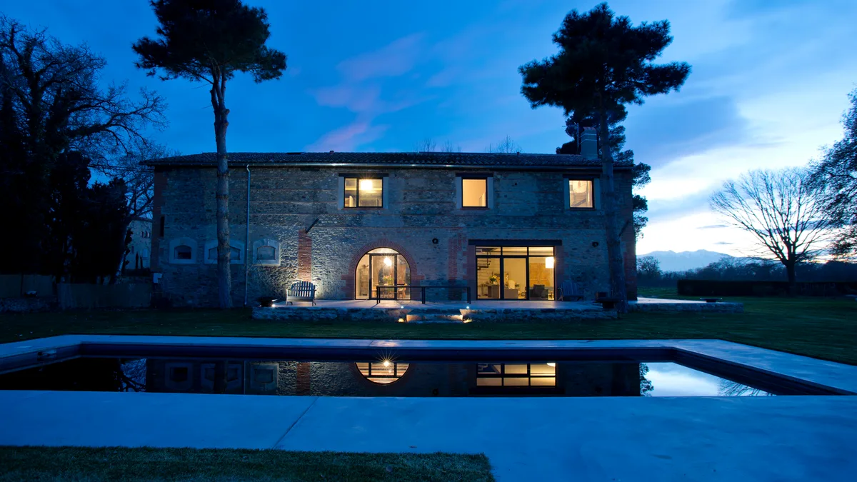 L'Écurie du Château de Villeclare, bâtisse en pierre aux fenêtres éclairées, se reflète dans un bassin à la tombée de la nuit.