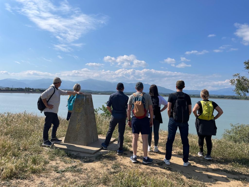 Groupe de randonneurs vus de dos au bord d'un lac, devant une chaîne de montagnes
