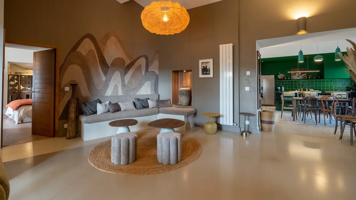 Un vaste séjour contemporain orné d'une fresque de montagnes, avec banquette d'angle, tabourets en pierre et suspension orange.