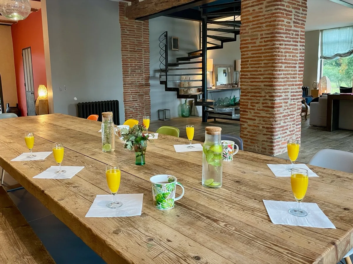Table en bois dressée, jus de fruits et carafe infusée au citron vert, salle à manger du lieu de séjour