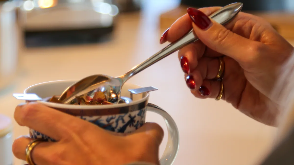 Au Château Montana, deux mains tiennent une tasse en faïence bleue et blanche, une cuillère prélevant les plantes d'une infusion.